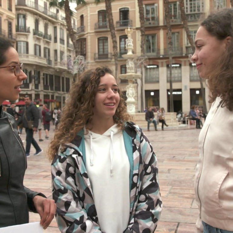 Drei junge Frauen stehen auf einem Platz und unterhalten sich.