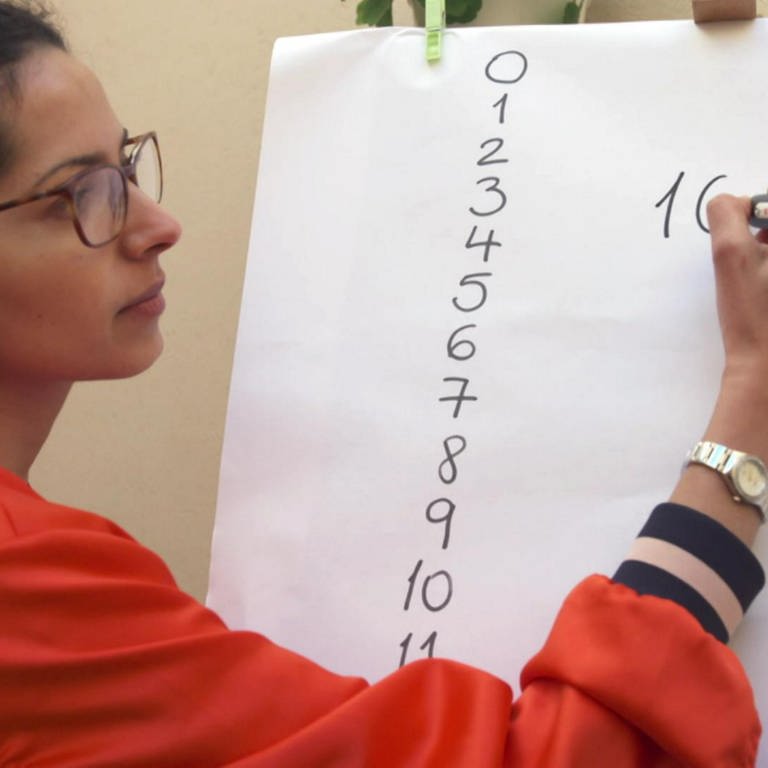 Eine Frau schreibt Zahlen an eine Tafel.